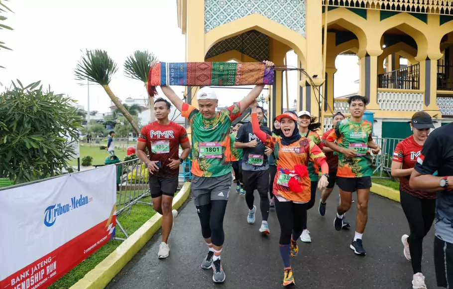 Gubernur Jawa Tengah Ganjar Pranowo tampak sumringah sambil mengangkat kain tenun Ulos saat tiba di garis finish Bank Jateng Friendship Run Borobudur Marathon 2022 di Medan, Sumatera Utara, pada Minggu, 25 September 2022.