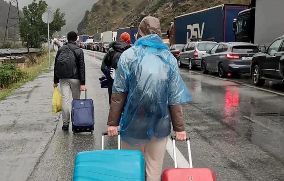 Orang-orang yang membawa barang bawaan berjalan melewati antrean panjang kendaraan dengan plat nomor Rusia di pos pemeriksaan pabean antara Georgia dan Rusia pada Minggu 25 September 2022.
