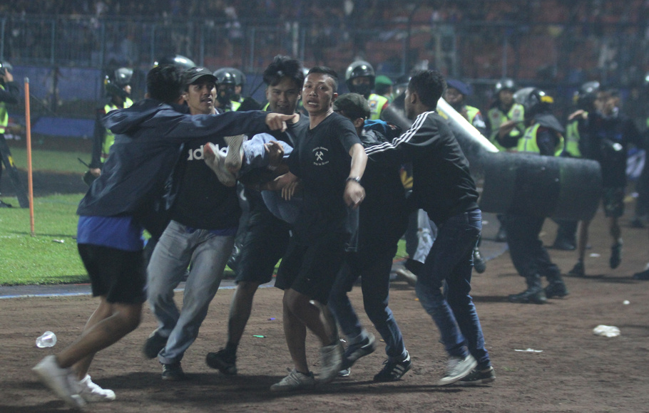 Sejumlah penonton membawa rekannya yang pingsan akibat sesak nafas terkena gas air mata yang ditembakkan aparat keamanan saat kericuhan seusai pertandingan Liga 1 antara Arema melawan Persebaya di Stadion Kanjuruhan, Malang, Sabtu, 1 Oktober 2022.