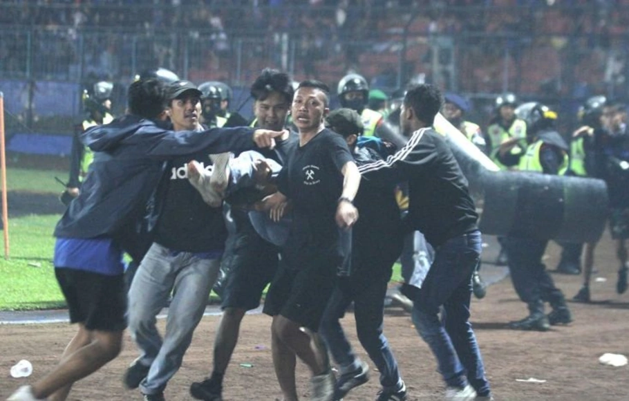 Sejumlah penonton membawa rekannya yang pingsan akibat sesak nafas terkena gas air mata yang ditembakkan aparat keamanan saat kericuhan usai pertandingan sepak bola BRI Liga 1 antara Arema melawan Persebaya di Stadion Kanjuruhan, Malang, Sabtu, 1 Oktober 2022.