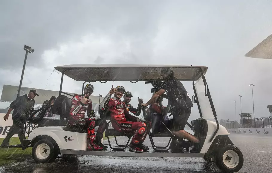 Fransesco Bagnaia, Jack Miller, dan Miguel Oliveira naik mobil golf di tengah hujan deras menuju podium setelah Grand Prix Thailand, 2 Oktober 2022.