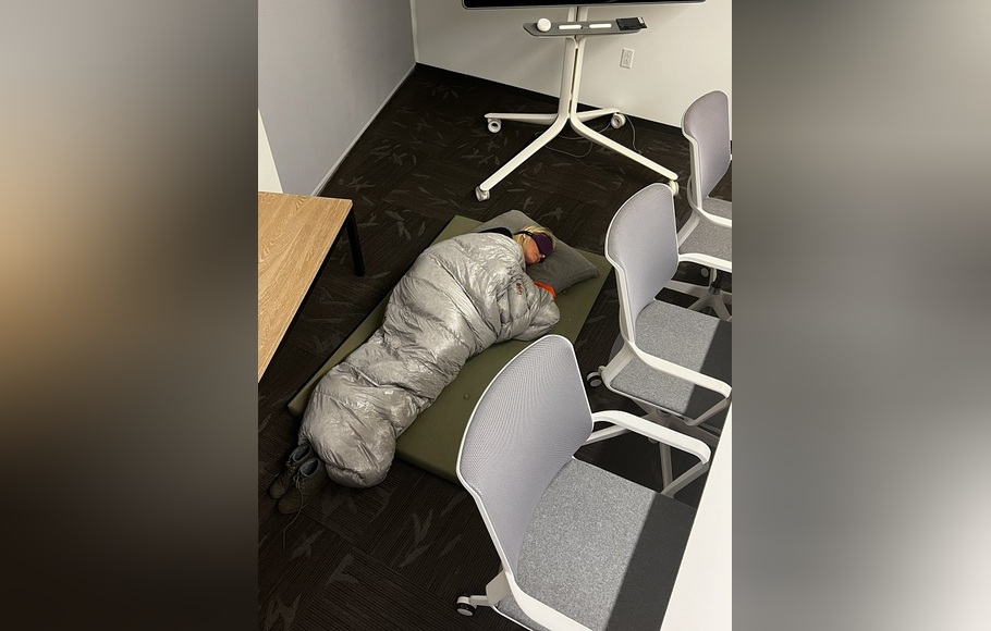 Direktur Manajemen Produk Twitter, Esther Crawford tertangkap kamera tidur berselimutkan sleeping bag dengan mata tertutup di antara meja-meja dan kursi kantor.