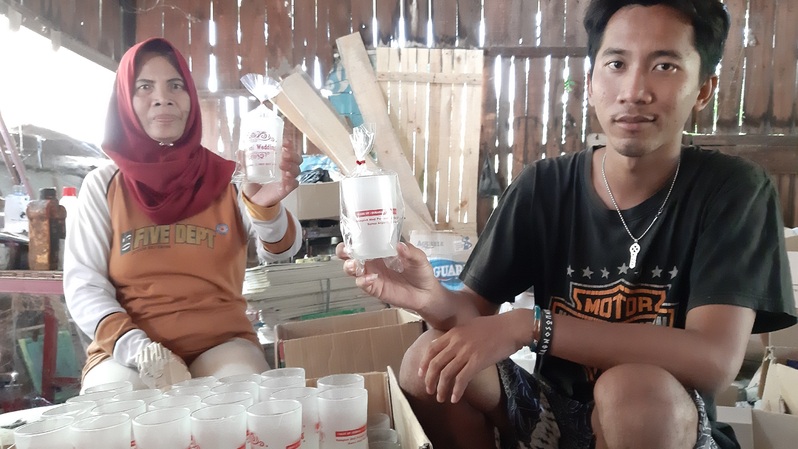 Kemi Yanti (kiri) dan putranya, Ahmad Bisri menunjukkan hasil sablon pada gelas souvenir yang akan dikirim ke Kalimantan, di workshop-nya yang terletak di Kecamatan Pedurungan, Semarang pada 21 Agustus 2019. (Foto: Investor Daily / Happy Amanda Amalia)

