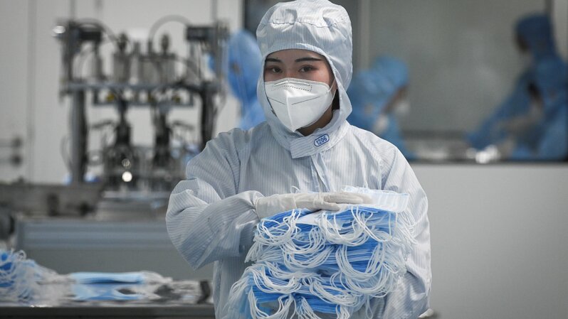 Seorang pekerja berpakaian alat pelindung diri (APD) lengkap menunjukkan tumpukan masker yang akan dikemas di Naton Medical Group, sebuah perusahaan produsen alat medis di Beijing, Tiongkok, pada 24 April 2020. ( Foto: WANG ZHAO / AFP )
