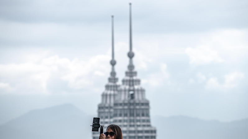 Seorang wanita sedang berswafoto  dengan latar belakang pemandangan Menara Kembar Petronas, dari Menara KL di Kuala Lumpur, Malaysia pada 24 Juli 2020. ( Foto: Mohd RASFAN / AFP )