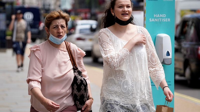 Para pejalan kaki memakai masker dengan diturunkan ke dagu, sedang berjalan melewati toko-toko di Oxford Street, di pusat kota London, pada 7 Juni 2021. ( Foto: NIKLAS HALLEN / AFP )