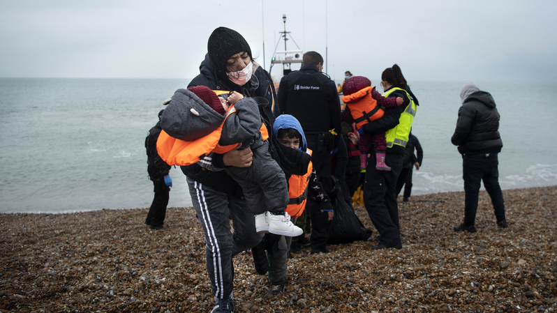 Seorang migran membawa anak-anaknya setelah dibantu turun dari sekoci RNLI (Royal National Lifeboat Institution), di sebuah pantai di Dungeness, pantai tenggara Inggris, pada 24 November 2021, setelah diselamatkan saat melintasi Selat Inggris (Channel). ( Foto: Ben Stansall / AFP )