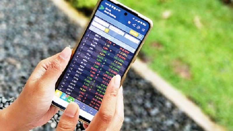 Trader memperhatikan pergerakan harga saham melalui ponselnya. Foto ilustrasi: Investor Daily/David Gita Roza