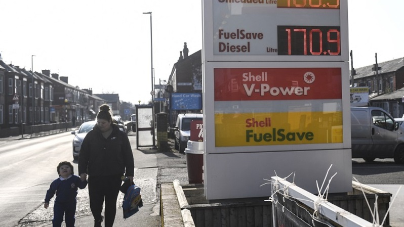 Warga berjalan melewati papan yang menunjukkan harga bahan bakar di stasiun pengisian Shell, di Manchester, Inggris. (FOTO: Oli SCARFF / AFP)
