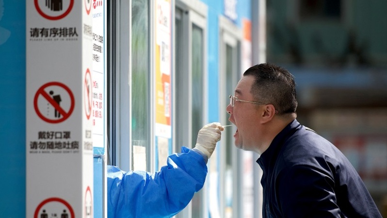 Seorang petugas kesehatan mengambil sampel swab dari seorang pria untuk tes virus corona Covid-19 di tempat pengumpulan swab di Beijing, Tiongkok pada 12 April 2022. (FOTO: NOEL CELIS / AFP)