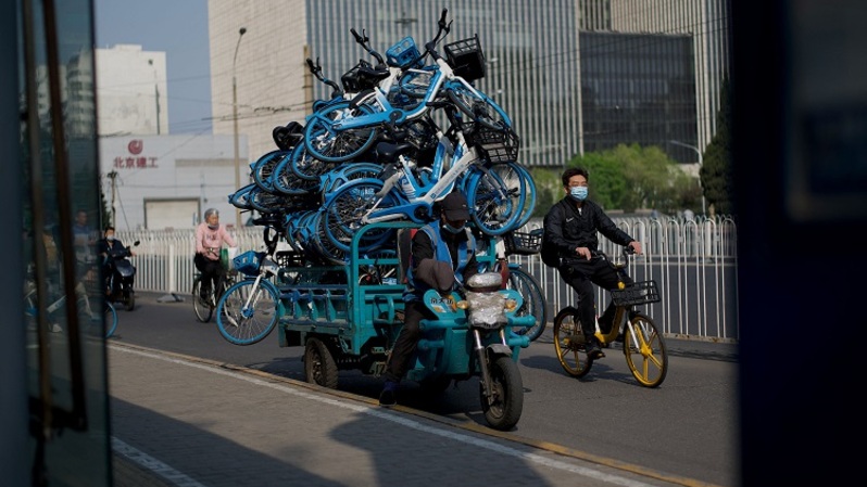 Seorang pekerja di perusahaan persewaan sepeda mengangkut sepeda dengan kendaraan roda tiga di Beijing pada 18 April 2022. (FOTO: NOEL CELIS / AFP)