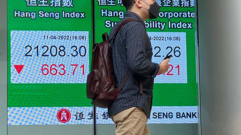 Seorang pria berjalan melewati papan yang menunjukkan angka Indeks Hang Seng di Hong Kong pada 11 April 2022. (FOTO: PETER PARKS / AFP)