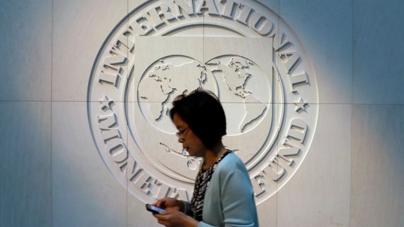 Seorang wanita berjalan melewati logo Dana Moneter Internasional (IMF) di kantor pusatnya di Washington, AS, beberapa waktu lalu. (FOTO: REUTERS / YURI GRIPAS)