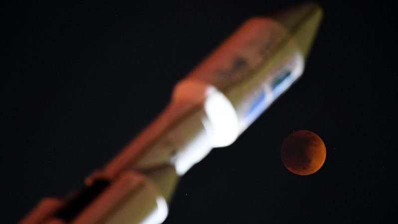 Blood moon terlihat selama gerhana bulan total oleh monumen bercahaya roket SpaceX Falcon Heavy di Hawthorne, California, AS pada 15 Mei 2022. (FOTO: PATRICK T. FALLON / AFP)