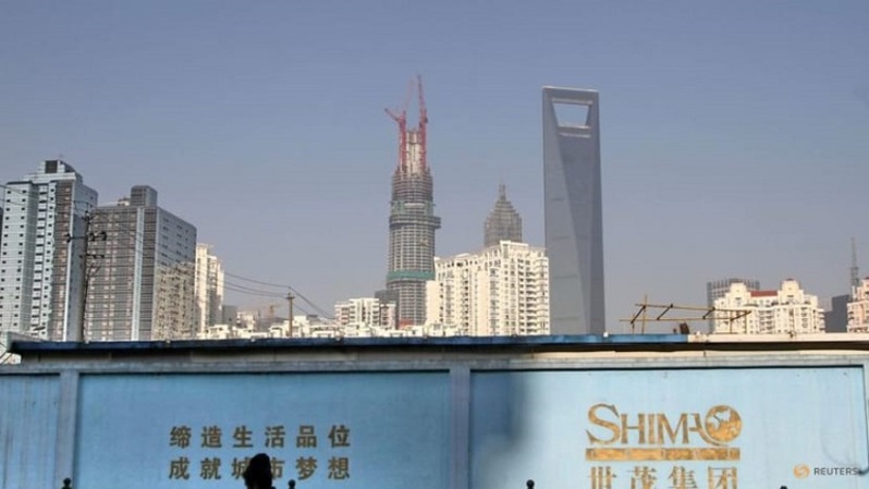 Seorang pria berjalan melewati dinding yang membawa logo Shimao Group, dengan bangunan tempat tinggal dan distrik keuangan Pudong terlihat di latar belakang di Shanghai, Tiongkok beberapa waktu lalu. (FOTO: Reuters)