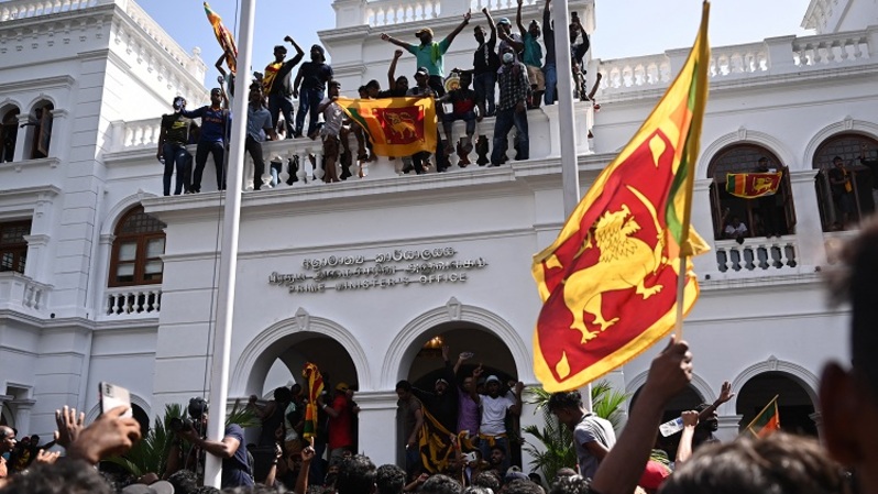 Demonstran meneriakkan slogan dan mengibarkan bendera Sri Lanka selama protes anti pemerintah di dalam gedung kantor perdana menteri Sri Lanka di Kolombo pada 13 Juli 2022. Ribuan pengunjuk rasa anti pemerintah menyerbu ke kantor Perdana Menteri Sri Lanka Ranil Wickremesinghe, beberapa jam setelah dia ditunjuk sebagai penjabat presiden, kata saksi. (FOTO: Arun SANKAR / AFP)