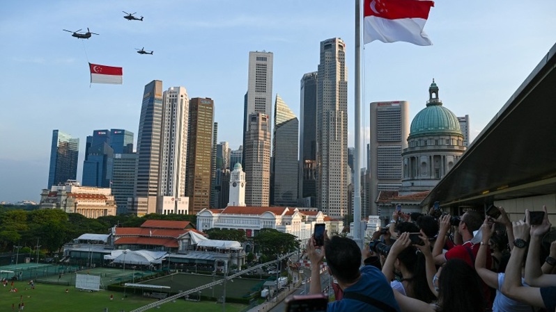 Penonton bersorak saat helikopter Chinook Angkatan Udara Singapura dikawal oleh helikopter Apache berparade dengan bendera Singapura untuk menandai Hari Nasional ke-57 negara itu di Singapura pada 9 Agustus 2022. (FOTO: Roslan RAHMAN / AFP)