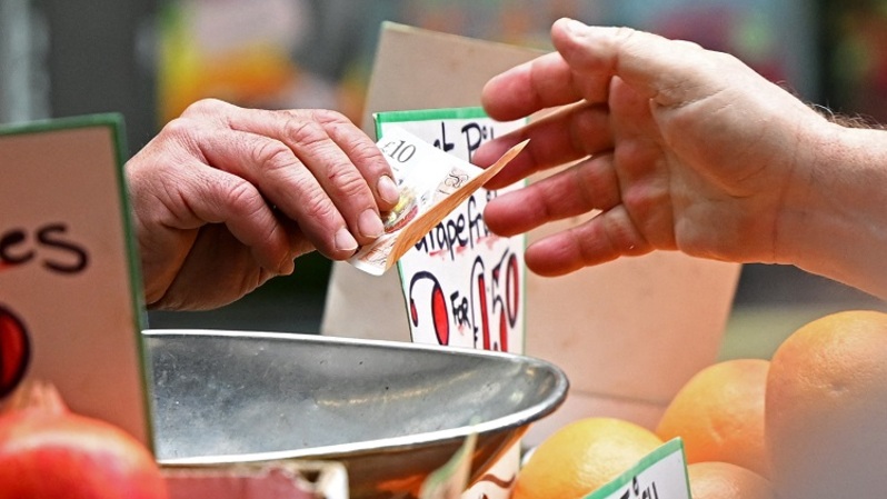 Pelanggan membayar buah dan sayurannya dengan uang kertas sepuluh pound sterling di kios pasar pedagang di London, Inggris. (FOTO: JUSTIN TALLIS / AFP)