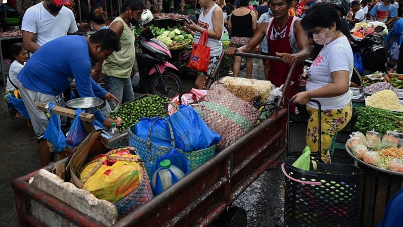 Seorang pria mendorong gerobak barang melalui pasar yang ramai di Manila .
