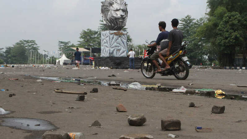 Seorang pengendara motor melintas diantara puing batu yang dilemparkan suporter dalam kerusuhan di Stadion Kanjuruhan, Malang, Jawa Timur, Minggu, 2 Oktober 2022. (Foto: Antara)