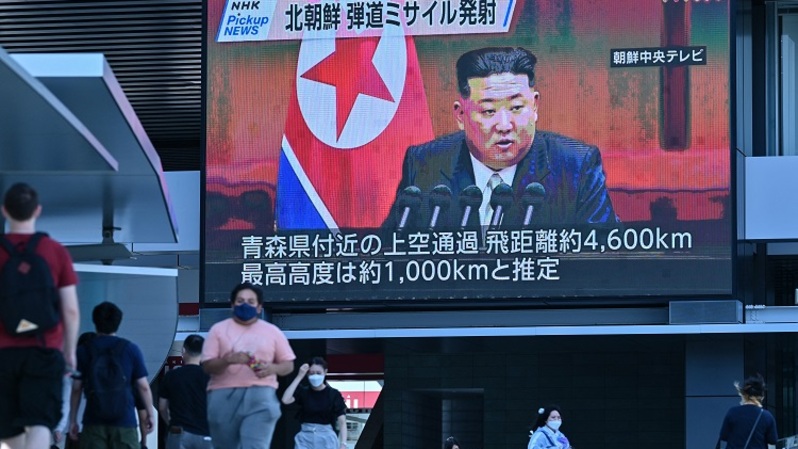 Pejalan kaki berjalan di bawah layar video besar yang menampilkan pemberitaan terkait pemimpin Korea Utara (Korut) Kim Jong Un di Tokyo, Jepang pada 4 Oktober 2022, setelah Korut meluncurkan rudal pada pagi hari yang memicu peringatan evakuasi ketika terbang di atas timur laut Jepang. (Foto: Richard A. Brooks / AFP)