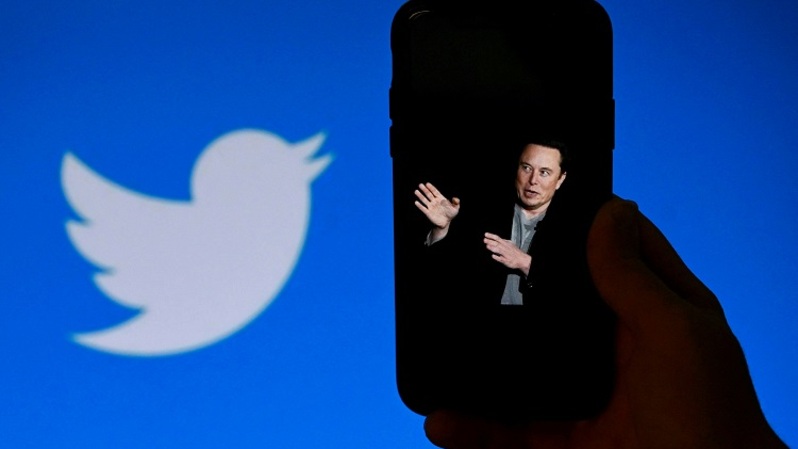 Ilustrasi Elon Musk dengan ponsel Apple dengan logo Twitter di latar belakang. (FOTO: OLIVIER DOULIER / AFP)