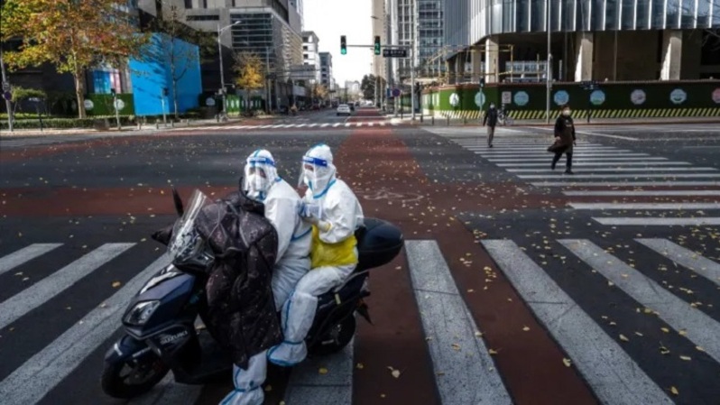 Pekerja pengendalian epidemi, yang melakukan tes asam nukleat mengenakan pakaian pelindung saat mereka bekerja untuk mencegah penyebaran Covid19, mengendarai skuter di jalan yang hampir kosong di Beijing, Tiongkok. (Foto: Kevin Frayer/Getty Images)