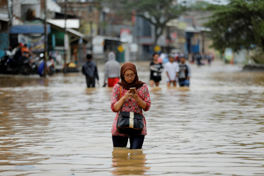 A woman uses her mobile phone while wading through a flooded street in Dayeuhkolot. (Reuters Photo/Darren Whiteside)
