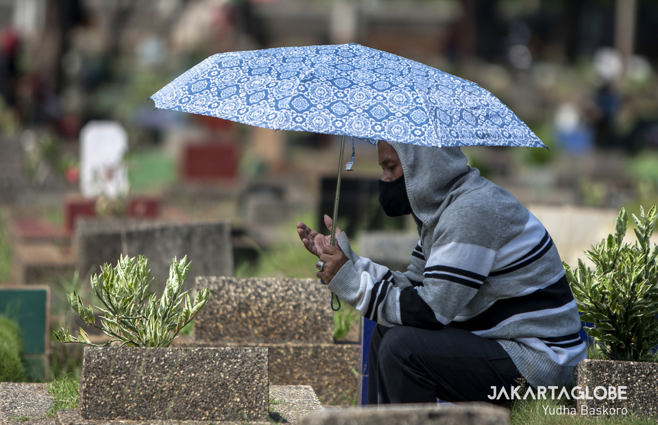 A man carrying umbrella, prays at Karet Tengsin public cemetery in Central Jakarta on Wednesday (22/04). (JG Photo/Yudha Baskoro)