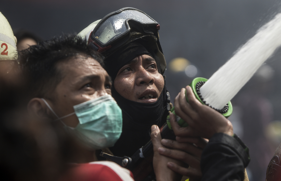 A man helps a firefighter as they try to extinguish the fire together in Manggarai, South Jakarta on Tuesday (07/07). (JG Photo/Yudha Baskoro)