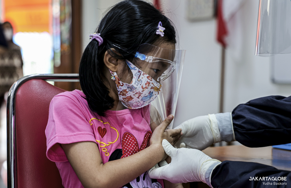 A child wearing health mask and face shield takes measles vaccine during child