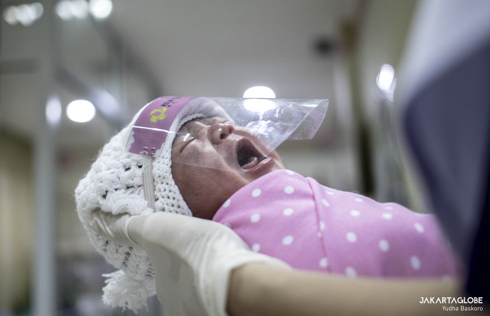 A nurse holds a newborn baby wearing a mini face shield at Tambak Children
