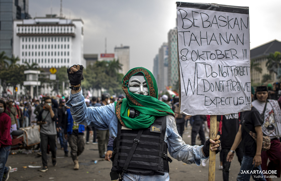 A protester wearing a Guy Fawkes mask carries a placard during a riot near Arjuna Wijaya Statue, also affectionally known as the Horse Statue, in Central Jakarta on October 13, 2020. (JG Photo/Yudha Baskoro)