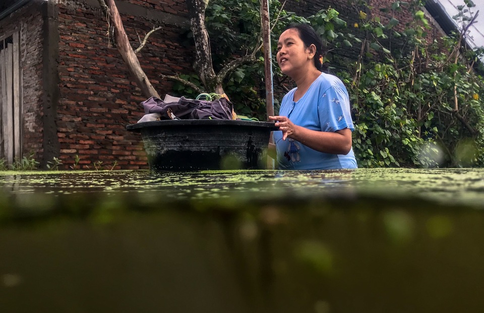 Warga menyelamatkan pakaian kering menggunakan ember saat melintasi jalan desa yang terendam banjir di Desa Sayung, Kecamatan Sayung, Kabupaten Demak, Jawa Tengah, Minggu (7/2/2021). Berdasarkan data dari Kantor Balai Desa Sayung, sebanyak 3.161 keluarga dengan total 10.297 jiwa yang tersebar di delapan dukuh di desa tersebut terendam banjir dengan variasi ketinggian sekitar 40-120 cm disebabkan oleh curah hujan tinggi serta meluapnya Sungai Dombo Sayung. ANTARA FOTO/Aji Styawan/rwa.