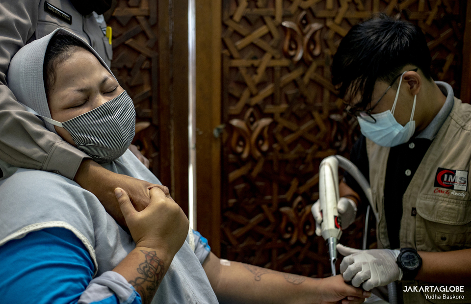 A woman reacts as a health worker removes her tattoo at the Assahara Mosque inside the West Jakarta Mayor
