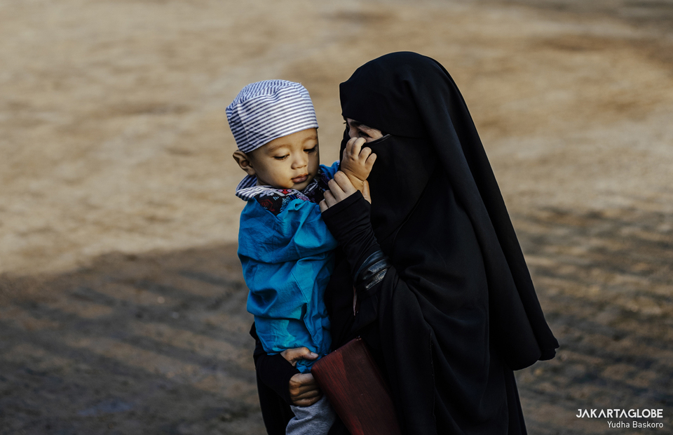 A woman carries her child during Idul Fitri prayer at Al-Bahrain Mosque inside Batavia