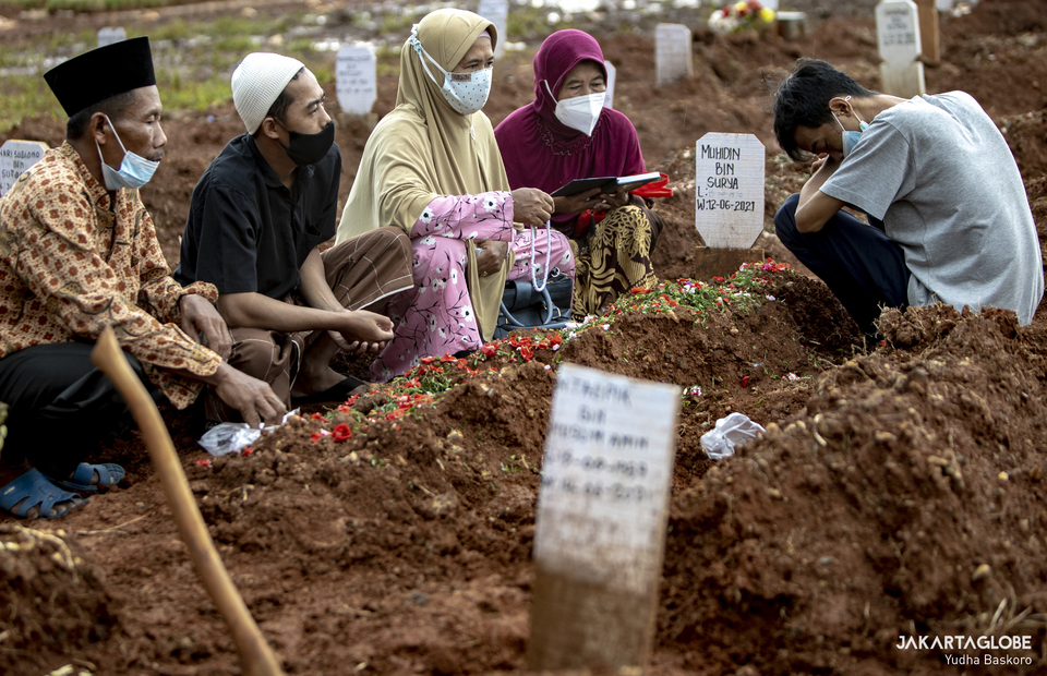 A family of the deceased pray next to the grave at Padurenan Cemetery in Bekasi, West Java on June 18, 2021. (JG Photo/Yudha Baskoro)