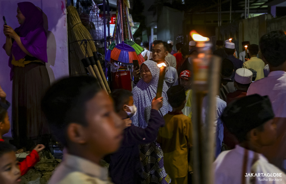 A woman smiles as children carrying torch pass in front of her during a parade for welcoming the holy month of Ramadhan at Cipedak, in South Jakarta on March 31, 2022. (JG Photo/Yudha Baskoro)