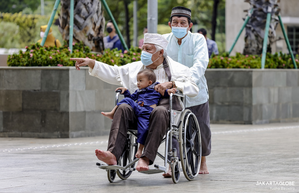 A man carries his grand son while sits on a wheel chair as he goes to Istiqlal Mosque in Central Jakarta on April 8, 2022. (JG Photo/Yudha Baskoro)