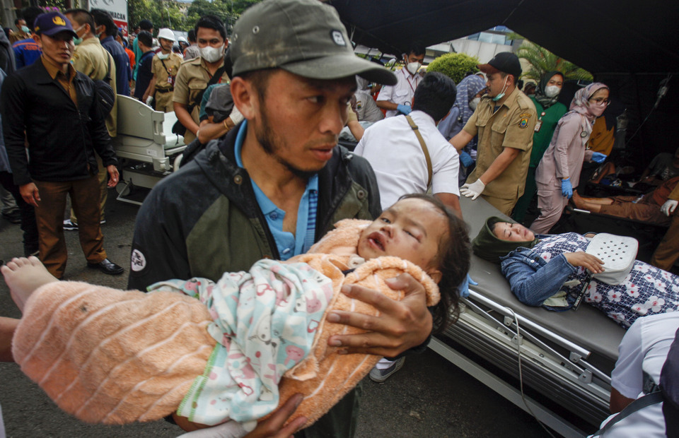 A man carries an injured child after an earthquake that rocked the West Java town of Cianjur on November 21, 2022. (Antara photo/Yulius Satria Wijaya)